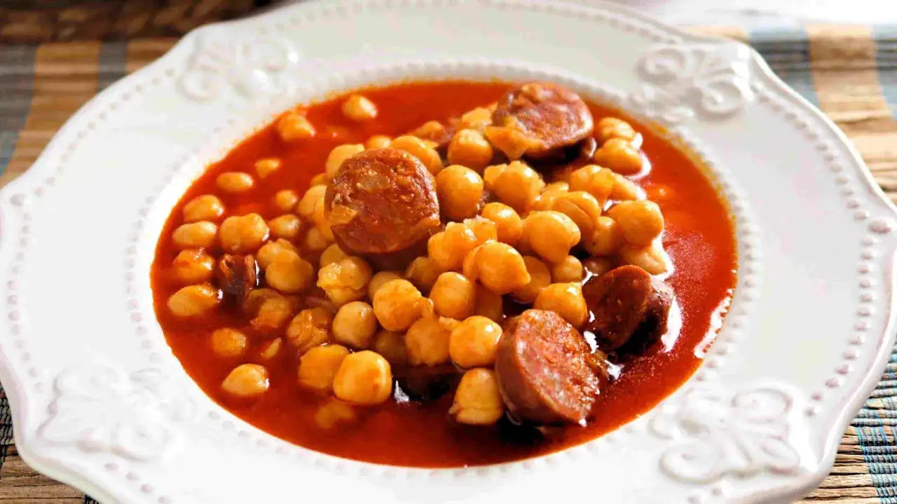 Un plato de garbanzos con chorizo en salsa roja, servido en una vajilla blanca con borde decorado.