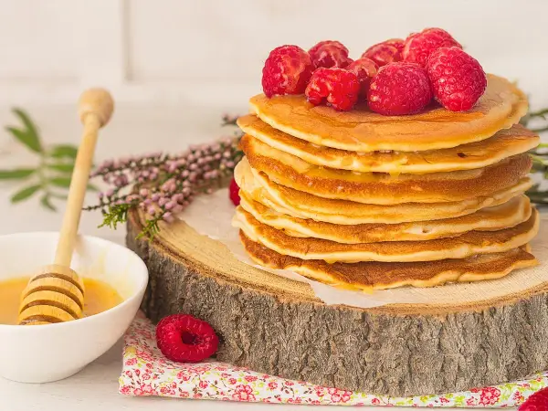 Una pila de tortitas de avena doradas, cubiertas con frambuesas frescas y miel, listas para disfrutar.