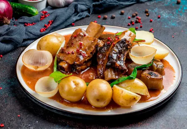 Costillas al horno con patatas, cebolla y un toque de vino blanco. Un plato jugoso y lleno de sabor.