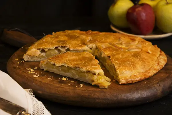 Empanada de manzana de la abuela, dorada y casera, servida en tabla de madera.